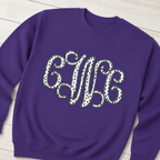 Styled flat lay of black dot vine monogram on Gildan 18000 Purple sweatshirt