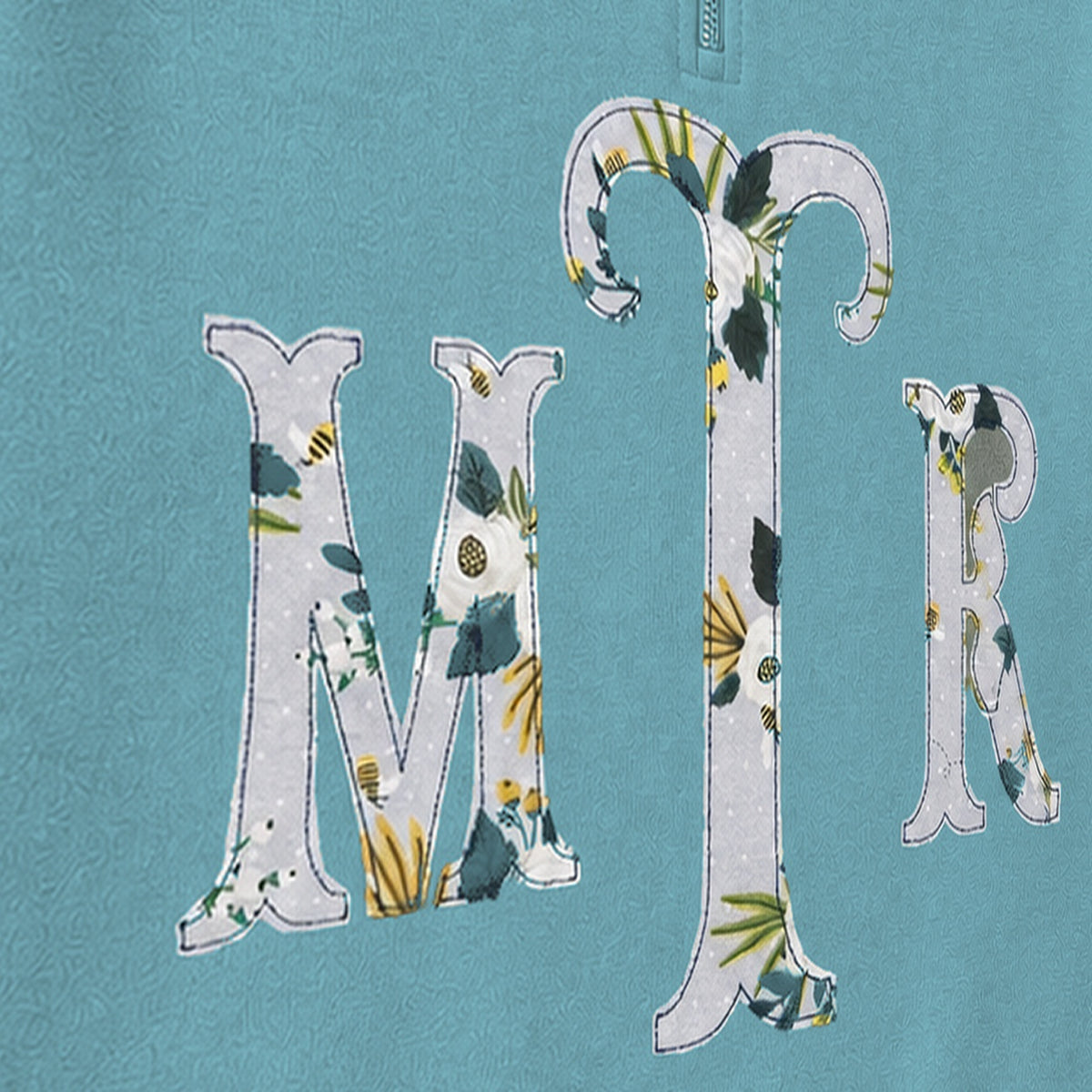Close-up of the embroidered design on a custom botanical floral serif monogram quarter zip pullover