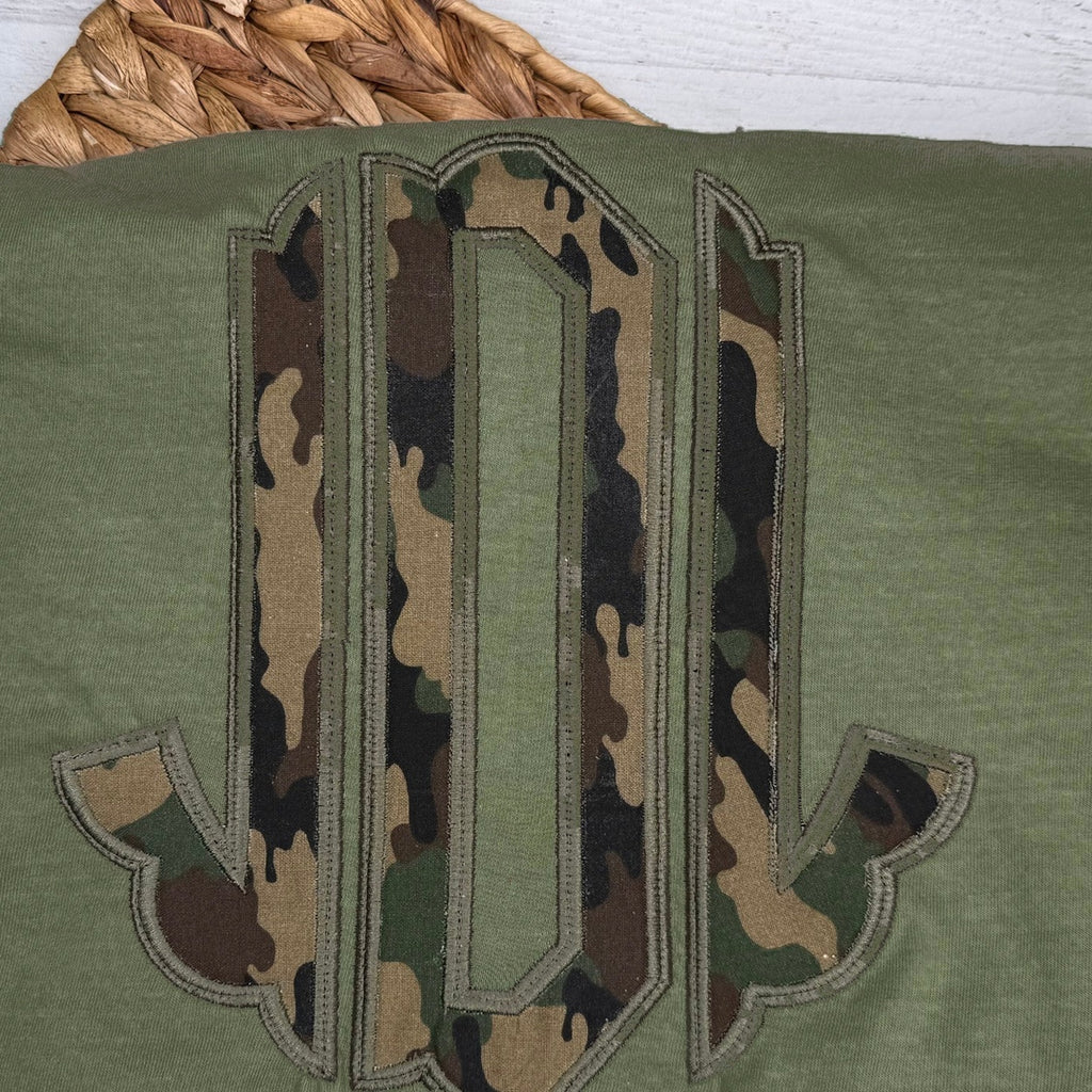 Close-up of the embroidered design on a camouflage circle monogram shirt